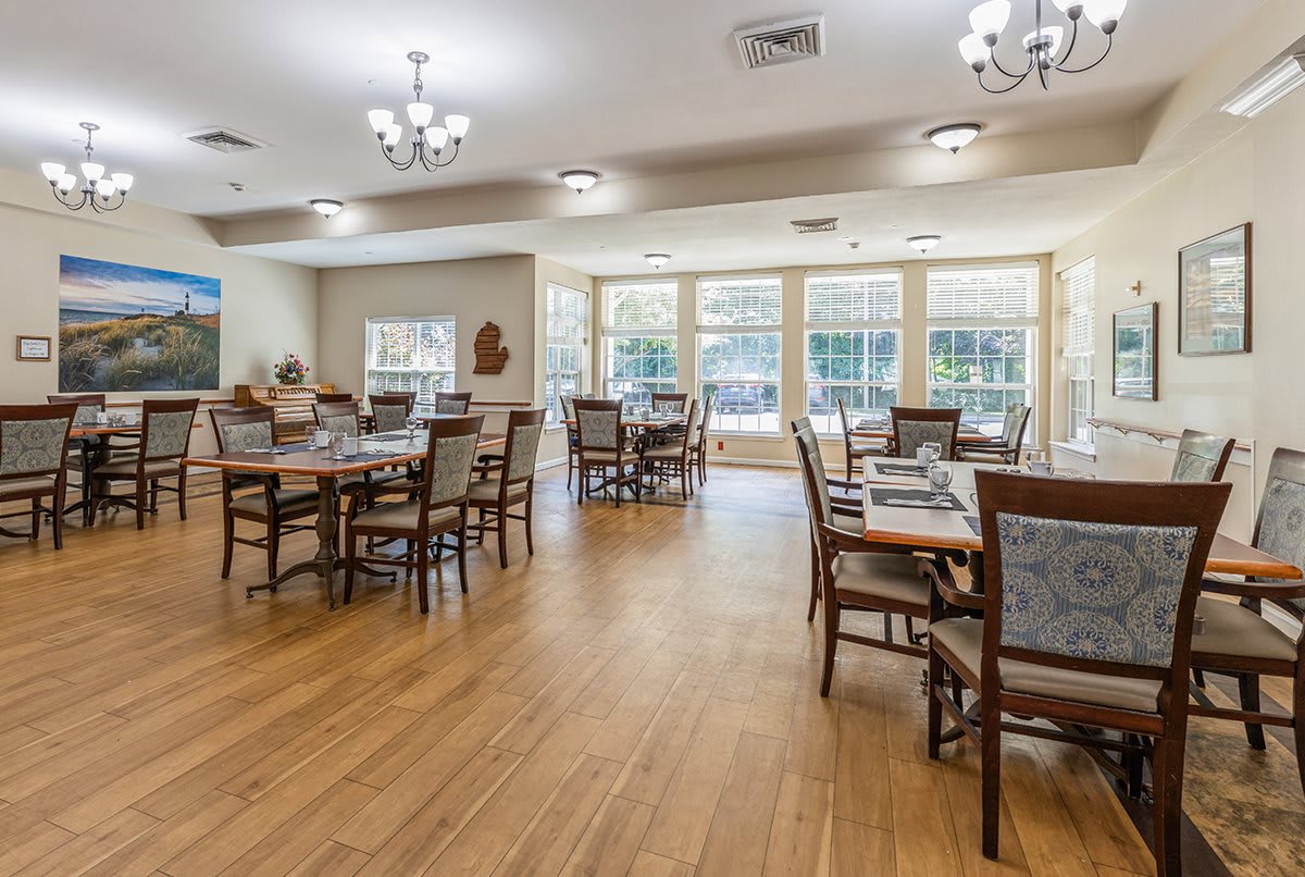 A spacious dining room with multiple tables and chairs, featuring wooden flooring and large windows.