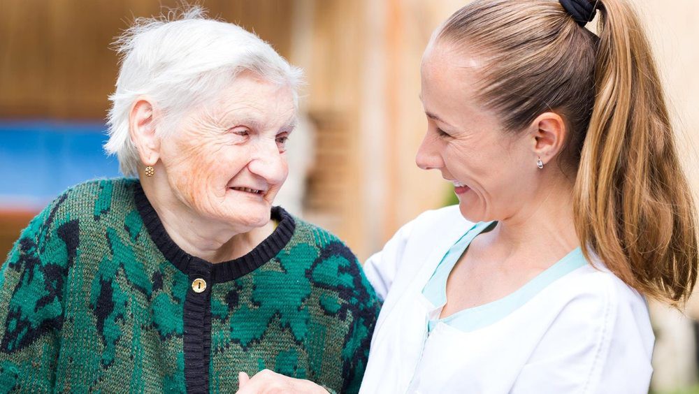 A caregiver smiling and interacting warmly with an elderly woman.