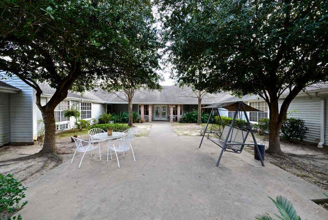 A cozy outdoor patio area with chairs and a swing set in front of a house surrounded by trees.