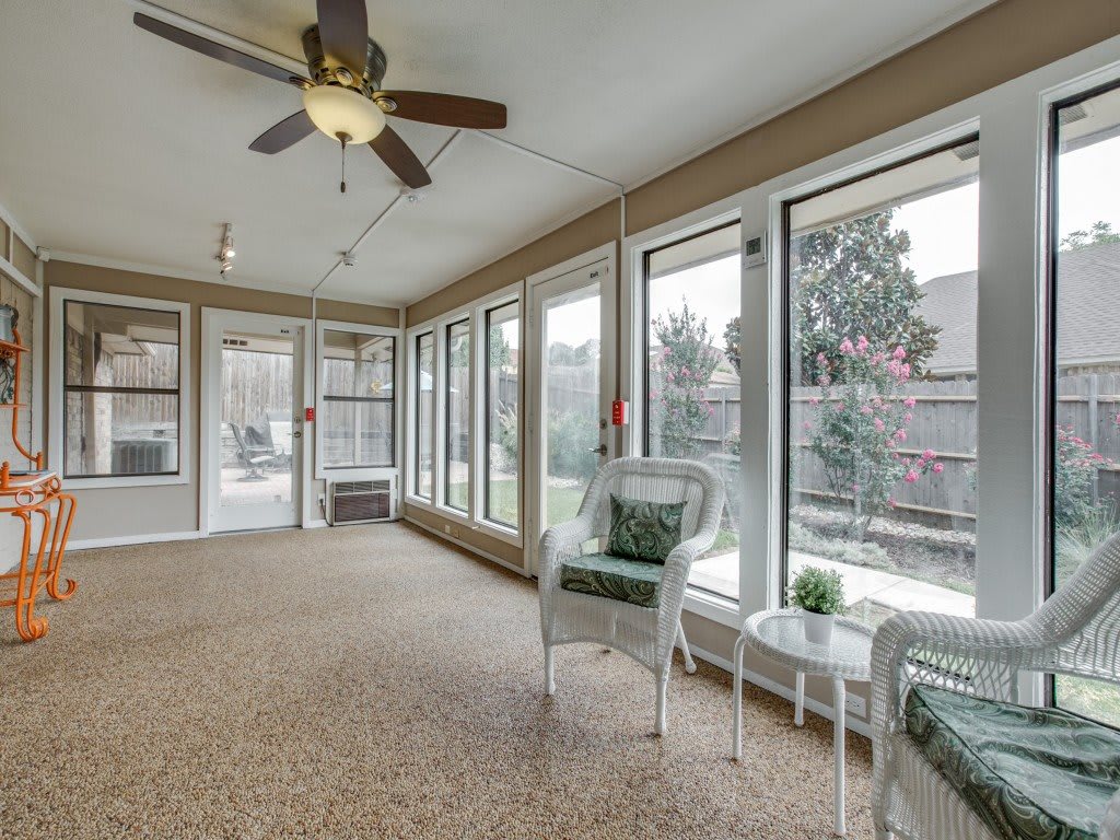 A bright sunroom with large windows, wicker chairs, and a ceiling fan.