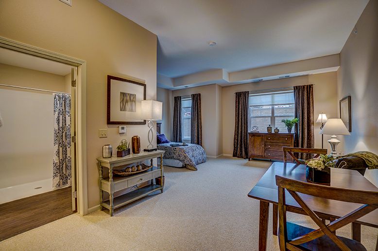 A cozy and well-furnished living room with a carpeted floor, dining table, and large windows.
