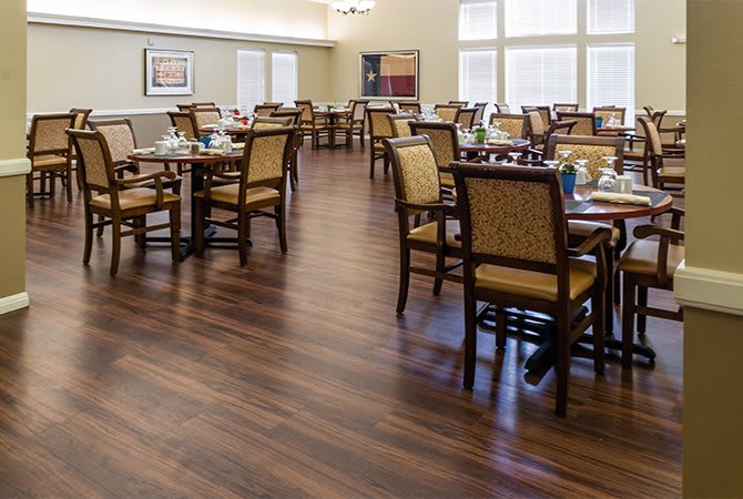 An empty dining room with neatly arranged tables and chairs on a wooden floor.