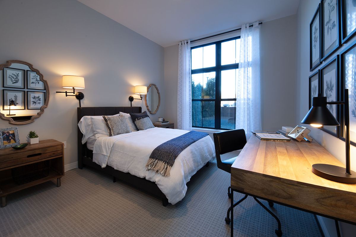 A cozy bedroom with a bed, desk, and large window.