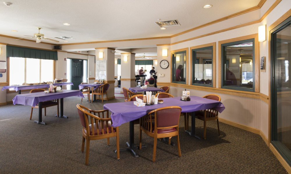 A spacious dining area with tables covered in purple tablecloths and wooden chairs.