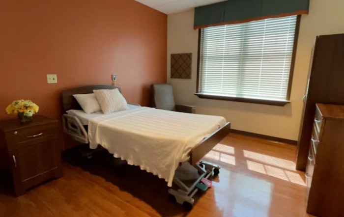 An empty hospital room with a bed and a window letting in natural light.