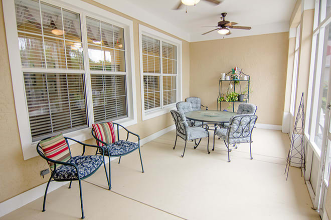 A cozy patio with outdoor furniture, including a table and chairs, ceiling fan, and decorative plants.