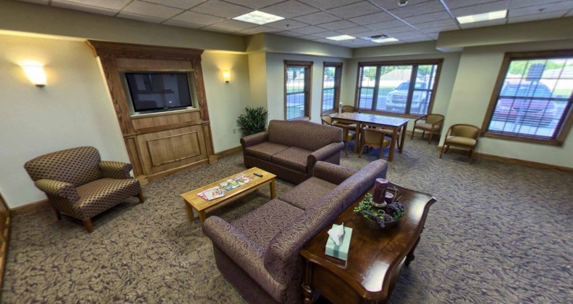A cozy living room with sofas, a coffee table, and a television, illuminated by natural light through large windows.