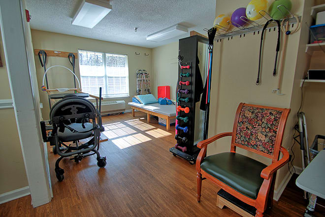 A well-lit physical therapy room equipped with various rehabilitation tools, including a walker and exercise balls.