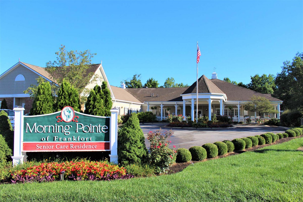Entrance to a picturesque building surrounded by well-maintained gardens and a prominent sign.