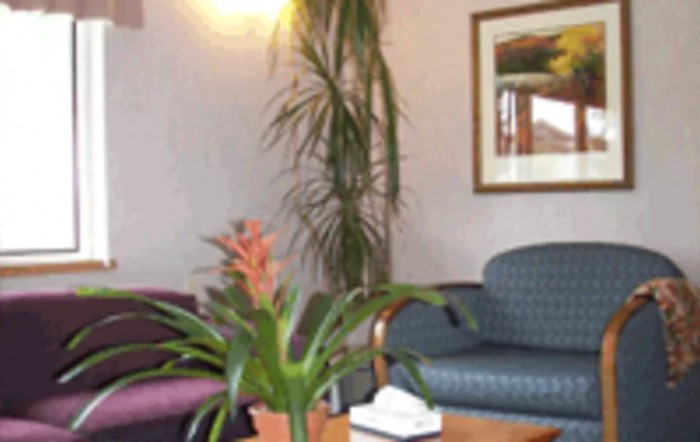 A cozy waiting room with a plant and artwork on the wall.