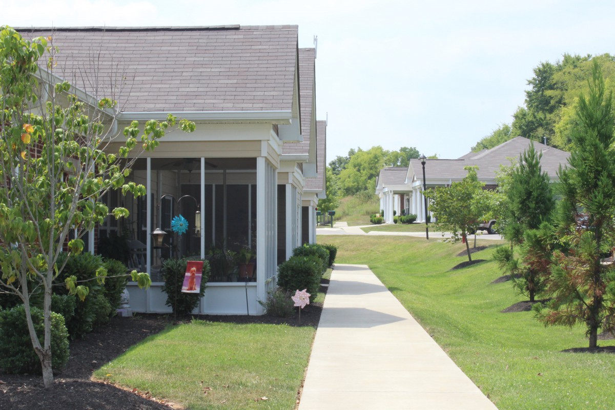 A suburban residential area with houses, a well-maintained lawn, and a sidewalk.