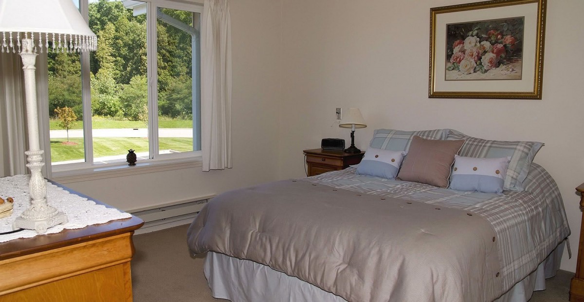 A cozy bedroom with a neatly made bed and a large window providing natural light.