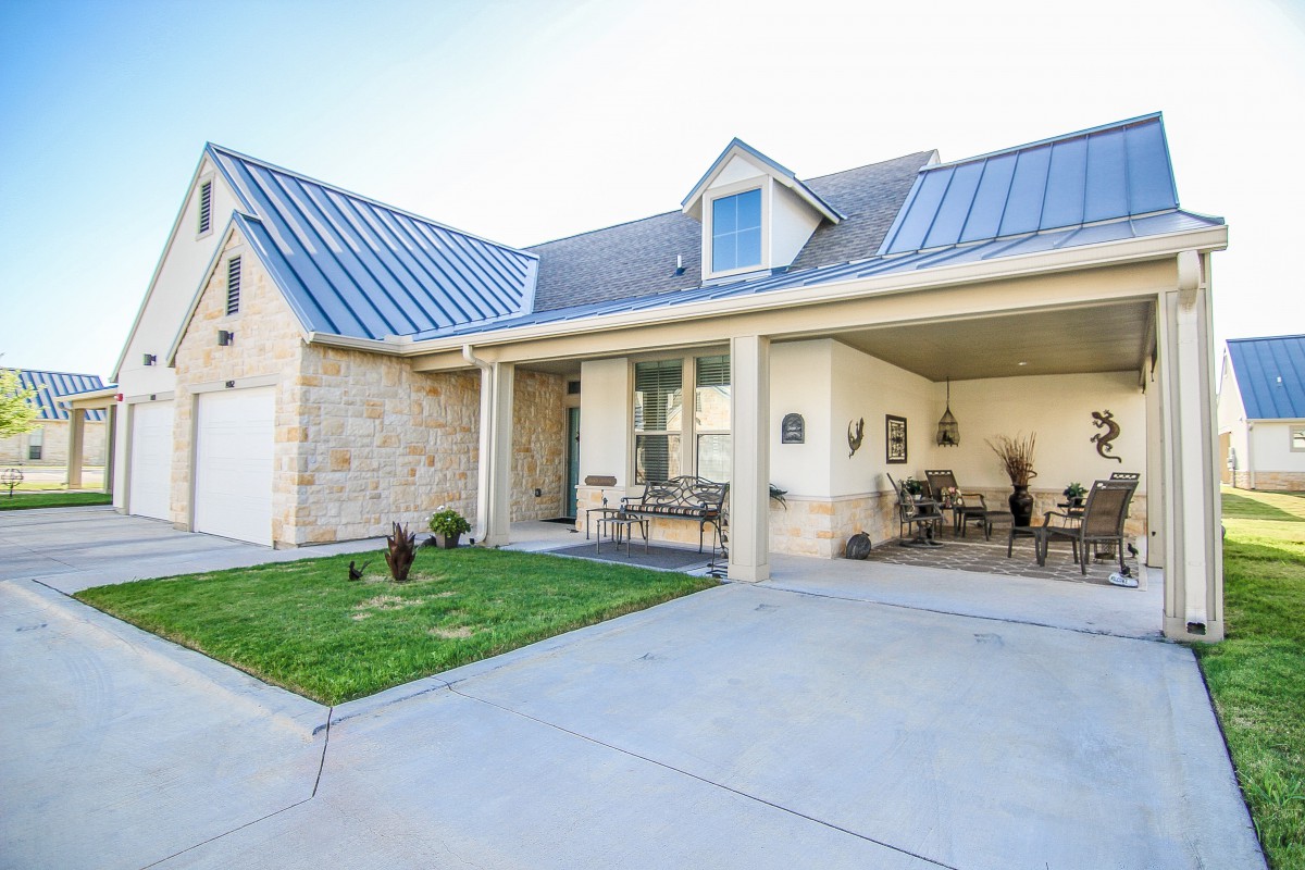 A modern house with a front yard and driveway, featuring a garage and outdoor seating area.