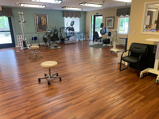 A spacious therapy room equipped with fitness machines and a polished wooden floor.