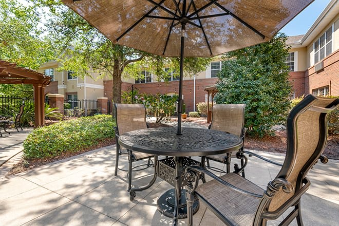 A sunny outdoor patio featuring a table and chairs with an umbrella in a garden setting.