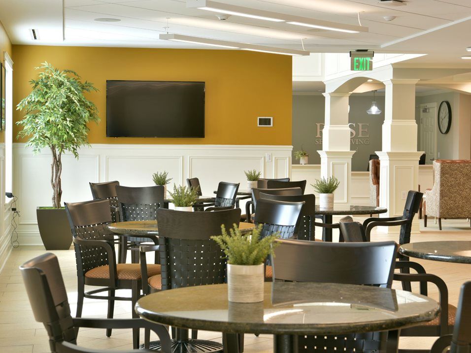 A modern dining area with tables and chairs, featuring a television and decorative plants.