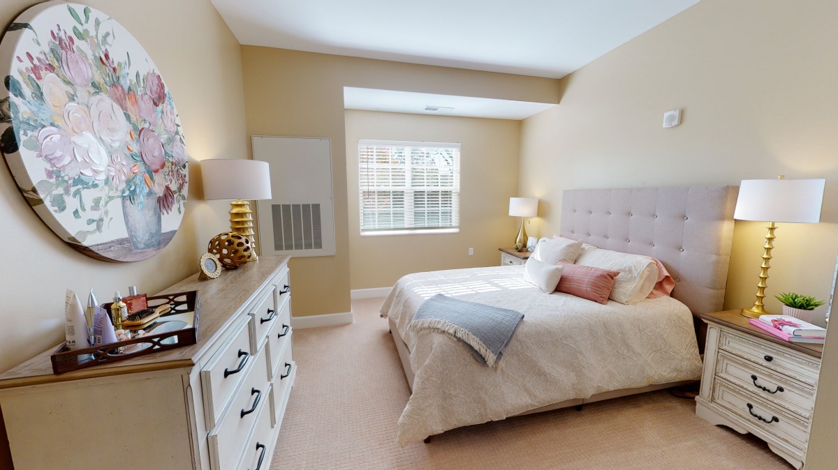 A cozy bedroom with neutral tones, featuring a bed, nightstands, and a large window allowing natural light.