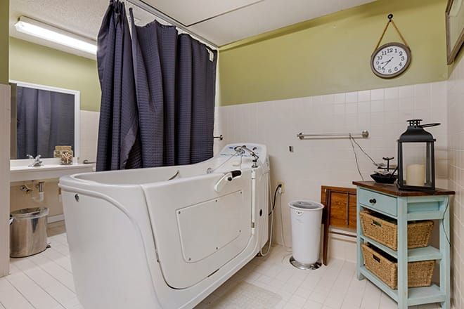 A bathroom featuring a walk-in bathtub with a dark curtain, sink, and wall-mounted clock.