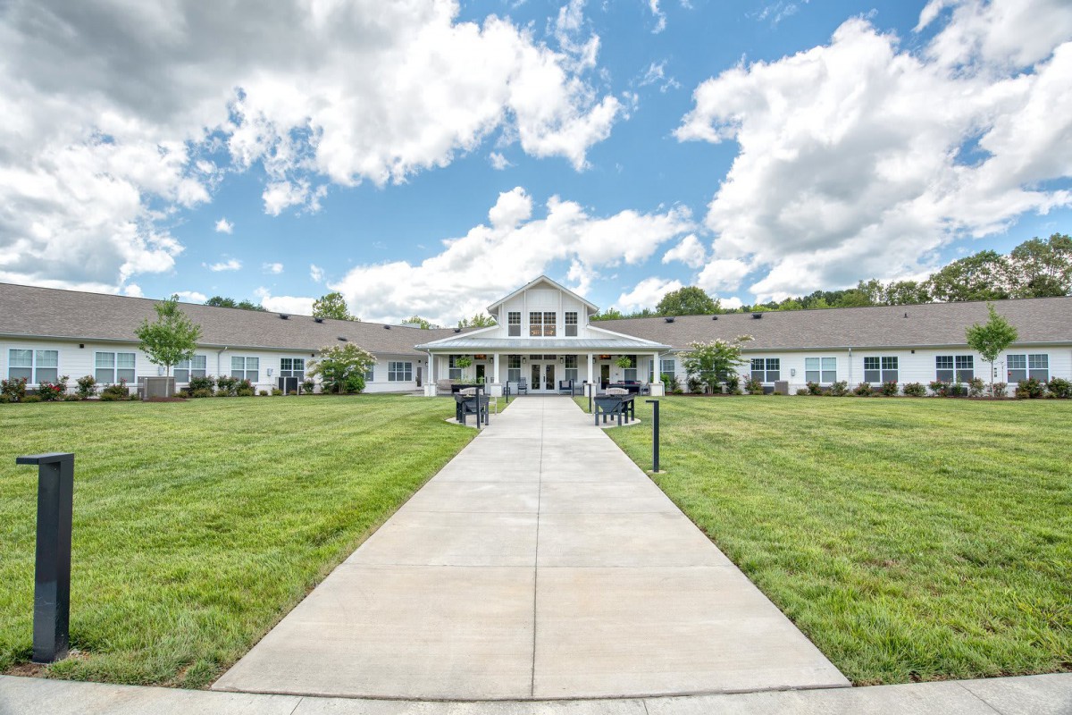 A large building with a symmetrical design sits under a partly cloudy sky, surrounded by a well-maintained lawn and a central pathway leading to the entrance.