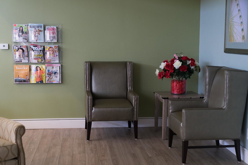 A quiet waiting room with a single chair, a table with flowers, and magazines on the wall.