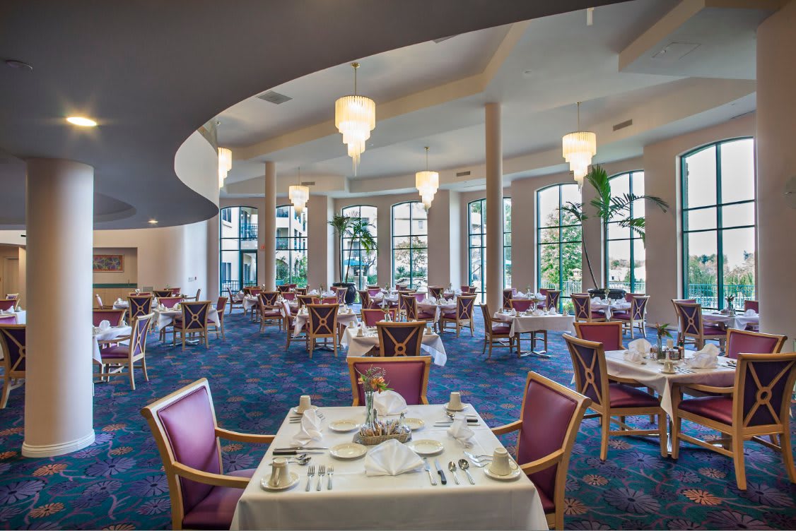 An elegant dining room with beautifully set tables and ample natural lighting through large windows.