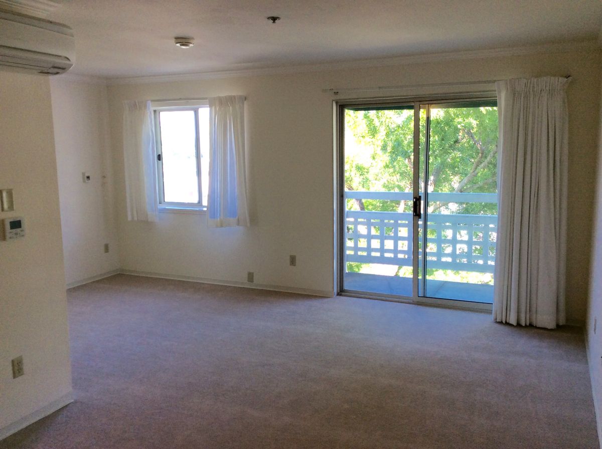 A bright living room with a window and sliding doors leading to a balcony.