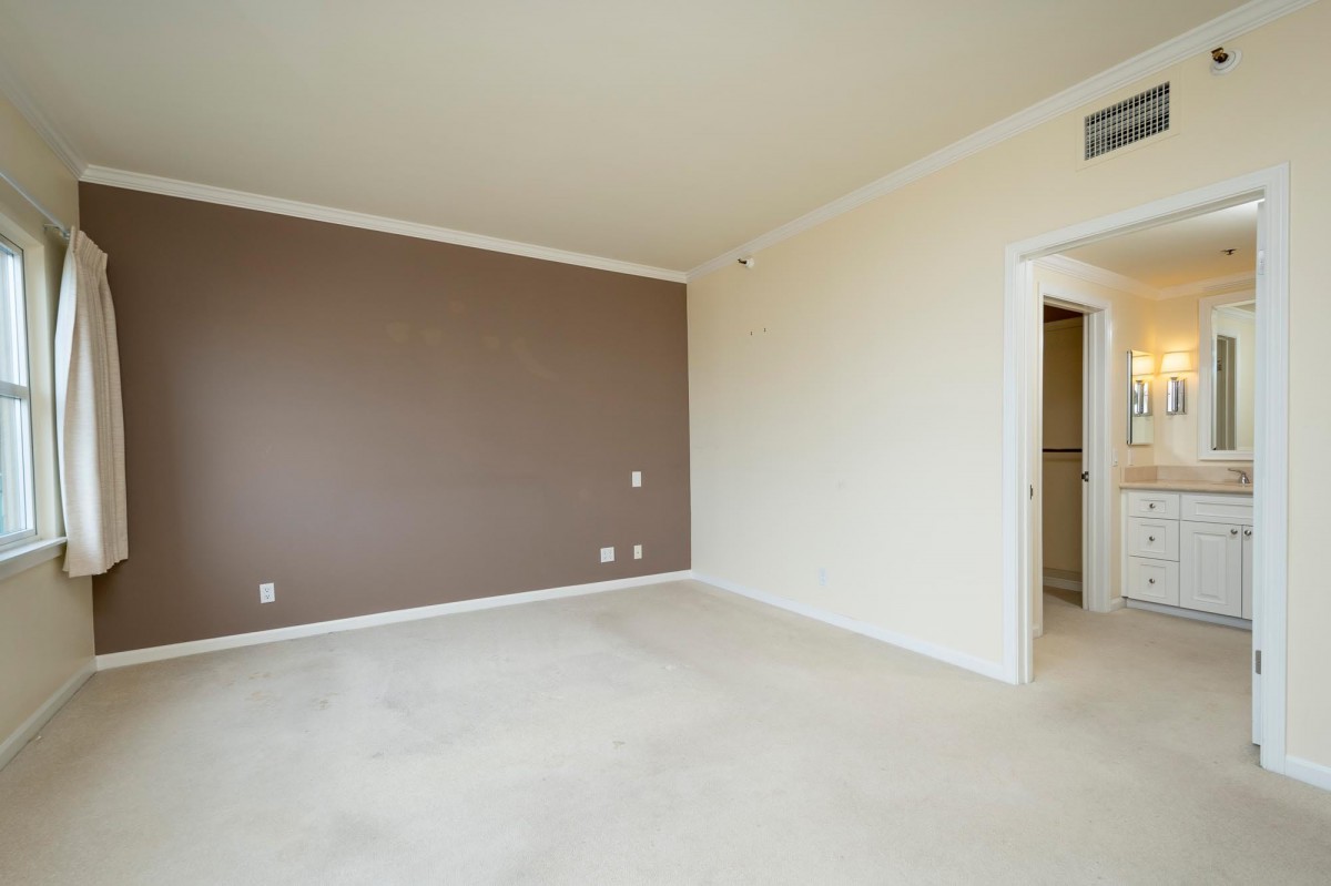 An empty room with beige walls and a carpeted floor, featuring a doorway to another area.