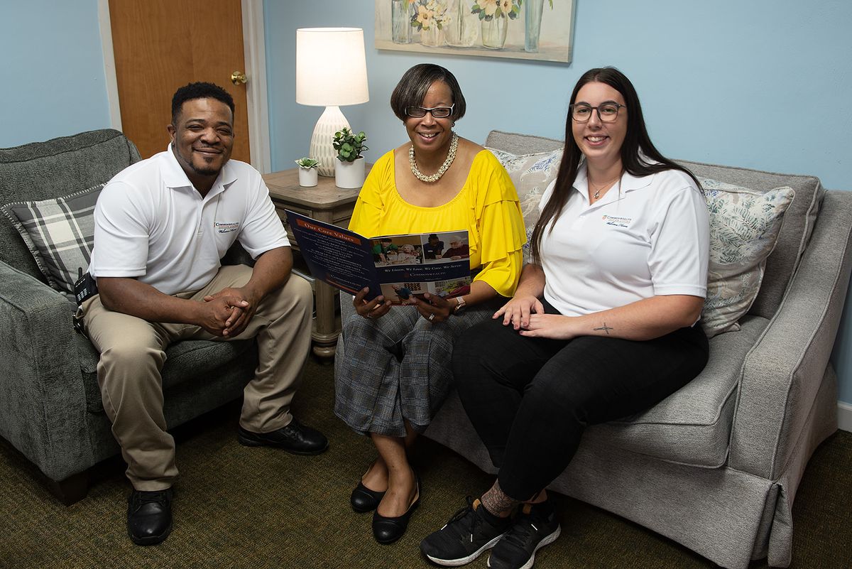 A group of three people sitting together on a sofa, smiling and looking at a laptop.