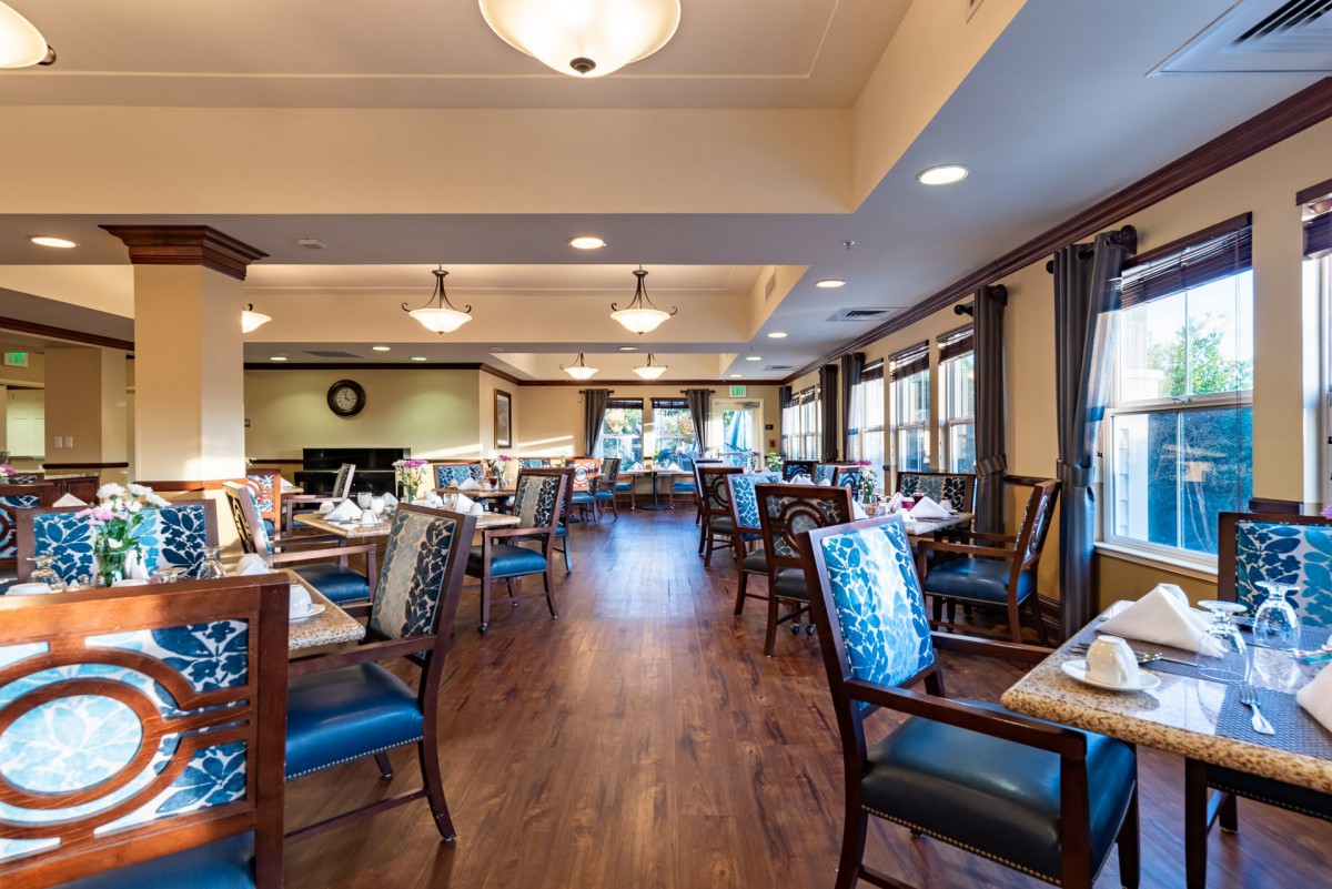 A spacious and elegantly designed restaurant dining room with neatly arranged tables and chairs, featuring warm lighting and wood flooring.