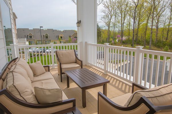 A cozy patio with cushioned chairs and a table, overlooking a parking area and greenery.