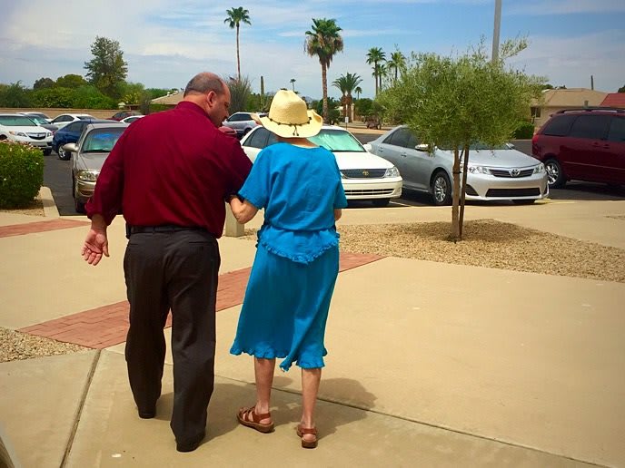 An elderly couple walking together in a parking lot on a sunny day.