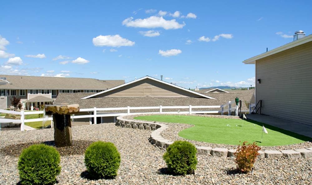 A landscaped garden with shrubs, a stone pathway, and a white fence under a clear blue sky.