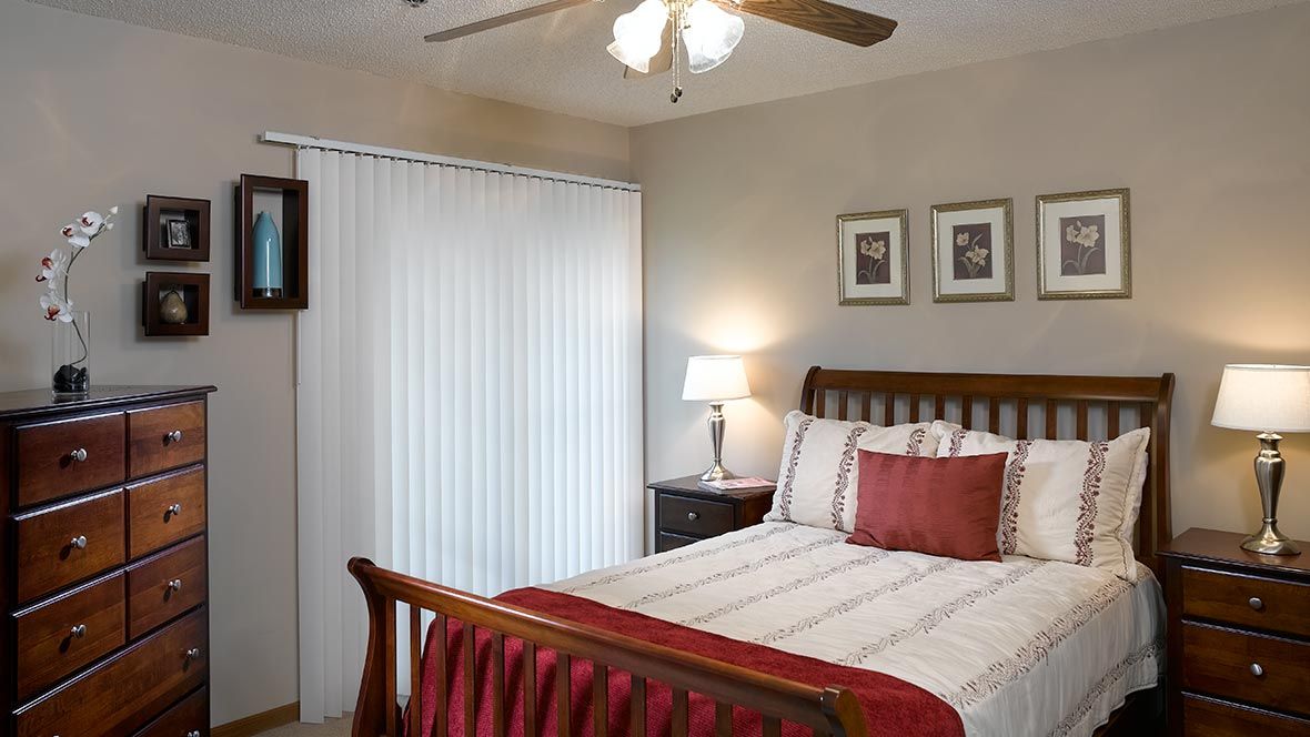 A cozy bedroom with a neatly made bed, lamp, and ceiling fan.