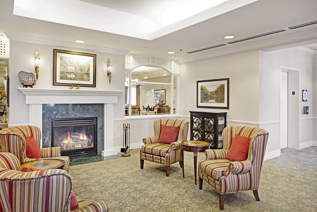A cozy living room with armchairs and a fireplace, adorned with artwork on the walls.