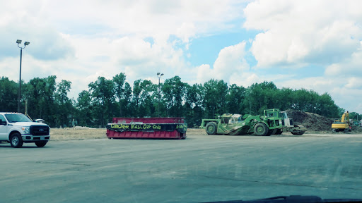 A vibrant pink and green heavy machinery parked outdoors, surrounded by trees and under a cloudy sky.
