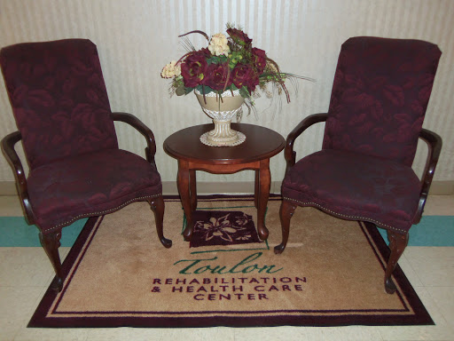 A cozy seating area with two burgundy chairs, a wooden table, and a floral arrangement on display.
