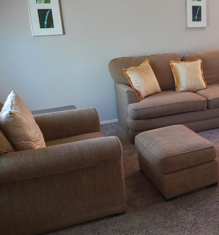A cozy living room with a sofa, armchair, and ottoman adorned with cushions.