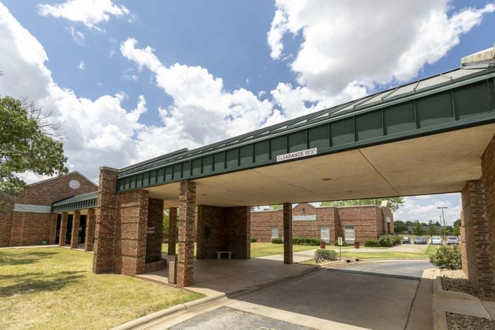 A building entrance with a covered driveway under a partly cloudy sky.