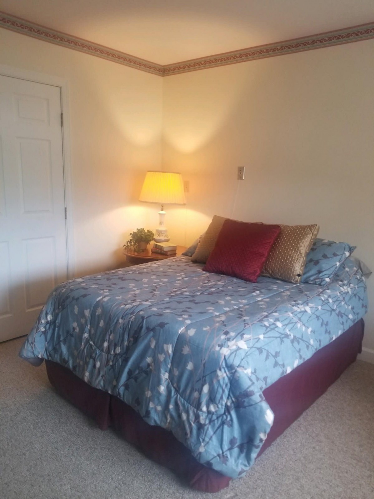 A cozy bedroom with a neatly made bed, accented by decorative pillows and illuminated by a warm lamp.