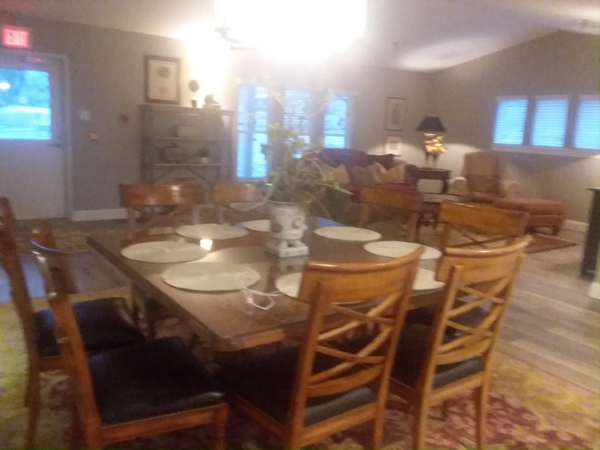 A cozy dining room with a set table, featuring wooden chairs and a floral centerpiece.