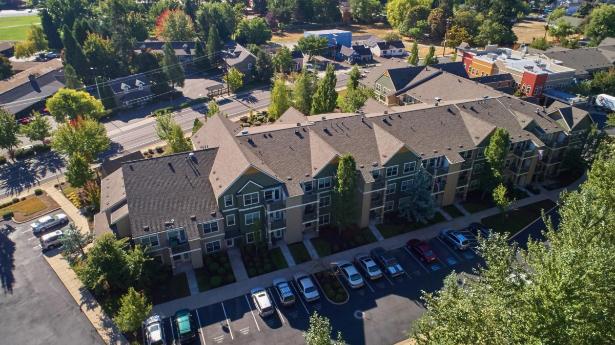 Aerial view of a residential apartment complex with a parking lot surrounded by trees.