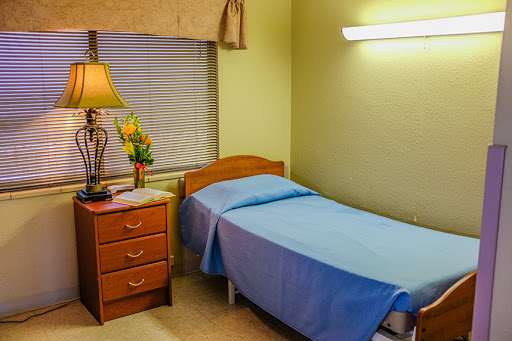 A simple and functional hospital room featuring a single bed, nightstand, and a lamp.