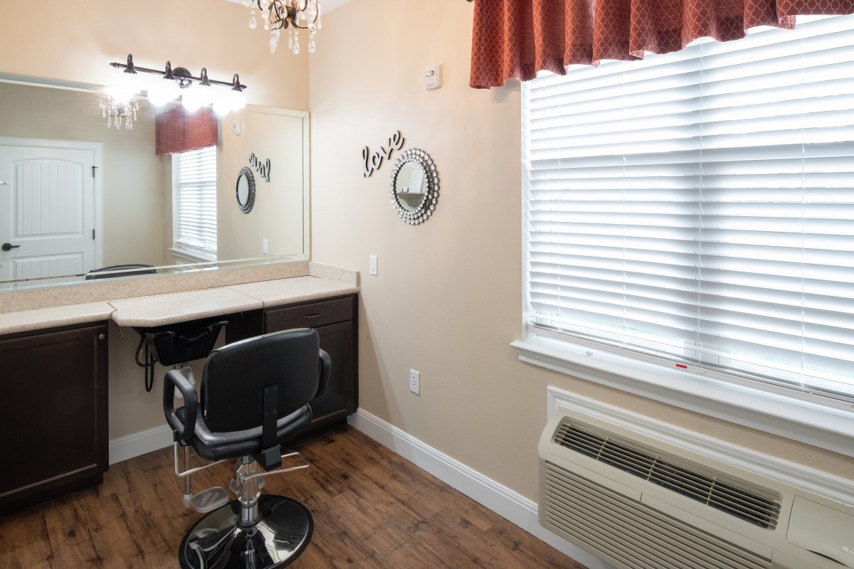 An empty hair salon room with a styling chair, mirror, and window.