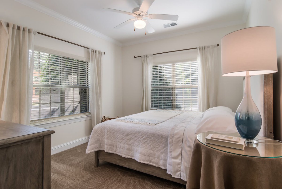 A cozy bedroom with a bed, curtains, and a ceiling fan.