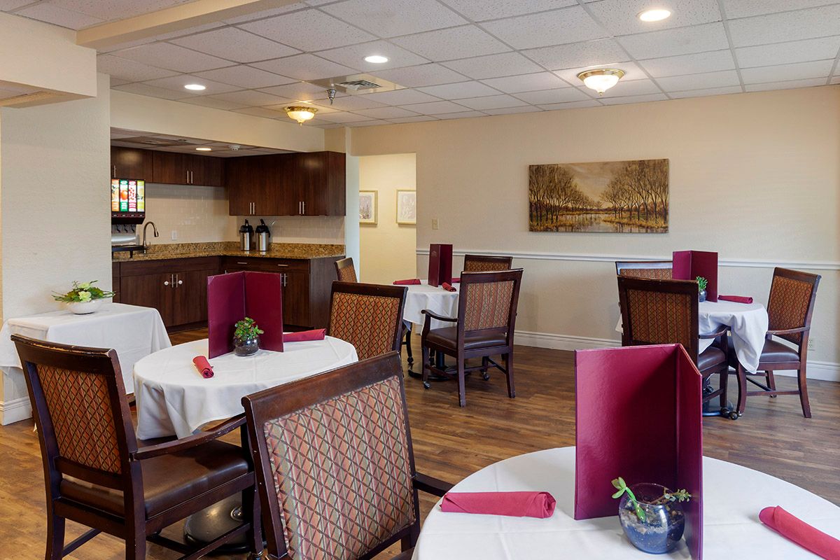 A cozy restaurant dining area with neatly arranged tables and chairs, featuring a glimpse of the kitchen in the background.