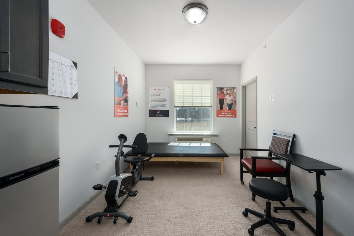A well-lit physical therapy room with exercise equipment, posters, and seating.