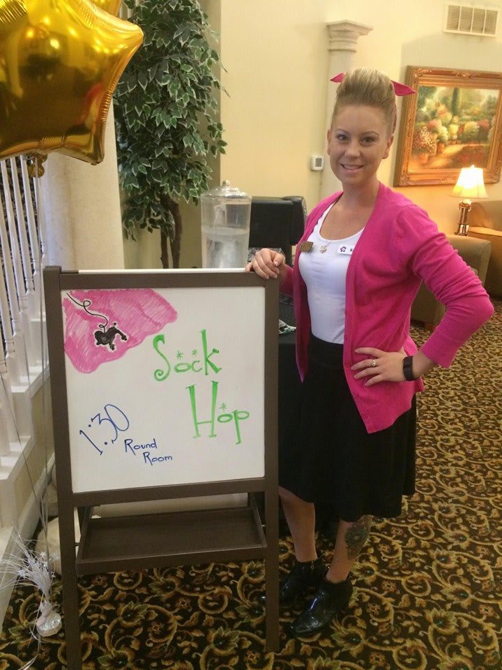 A woman stands next to a decorated sign indoors.