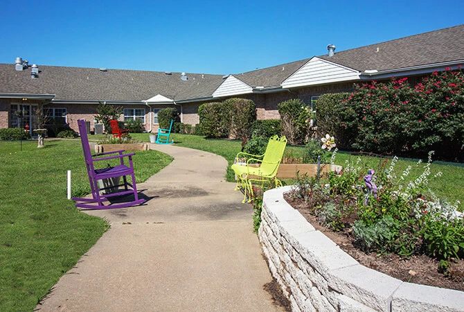 A serene garden pathway with colorful chairs and lush greenery.