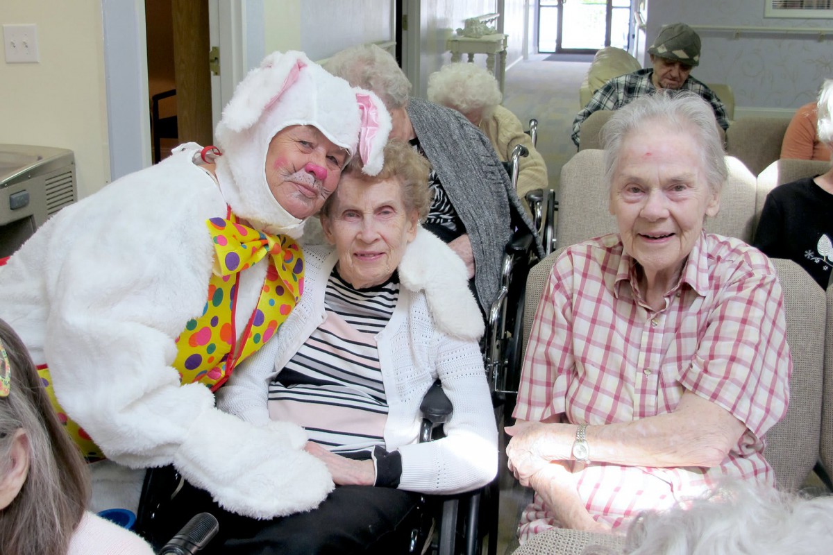 A person in a bunny costume poses with elderly residents in a nursing home, sharing a joyful moment.