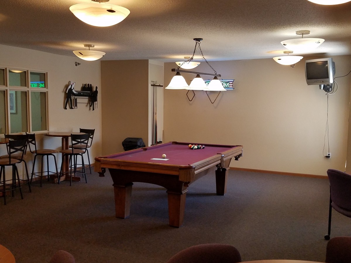 A cozy recreational room featuring a pool table with overhead lighting and seating areas.
